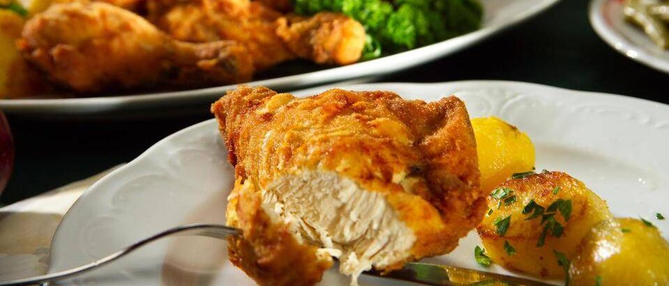 Zwei weiße Teller mit gebratenem Hähnchen, Brokkoli, Kartoffeln und Äpfeln auf einem Tisch mit einer Gabel und einem Messer auf dem vorderen Teller.