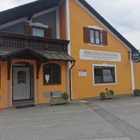 Ein orangefarbenes Gebäude mit dem Namen Gasthaus Gressmichl. Vor dem Eingang stehen Blumentöpfe. Ein Coca-Cola-Schild ist an der Wand neben der Tür.