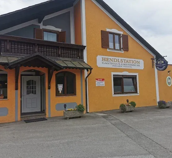 Ein orangefarbenes Gebäude mit dem Namen Gasthaus Gressmichl. Vor dem Eingang stehen Blumentöpfe. Ein Coca-Cola-Schild ist an der Wand neben der Tür.