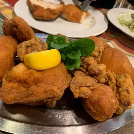 Gebratenes Hühnchen auf einem Teller mit einer Zitronenscheibe und grünen Blättern. Ein weiterer Teller mit Salat und Hühnchen.