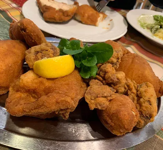 Gebratenes Hühnchen auf einem Teller mit einer Zitronenscheibe und grünen Blättern. Ein weiterer Teller mit Salat und Hühnchen.