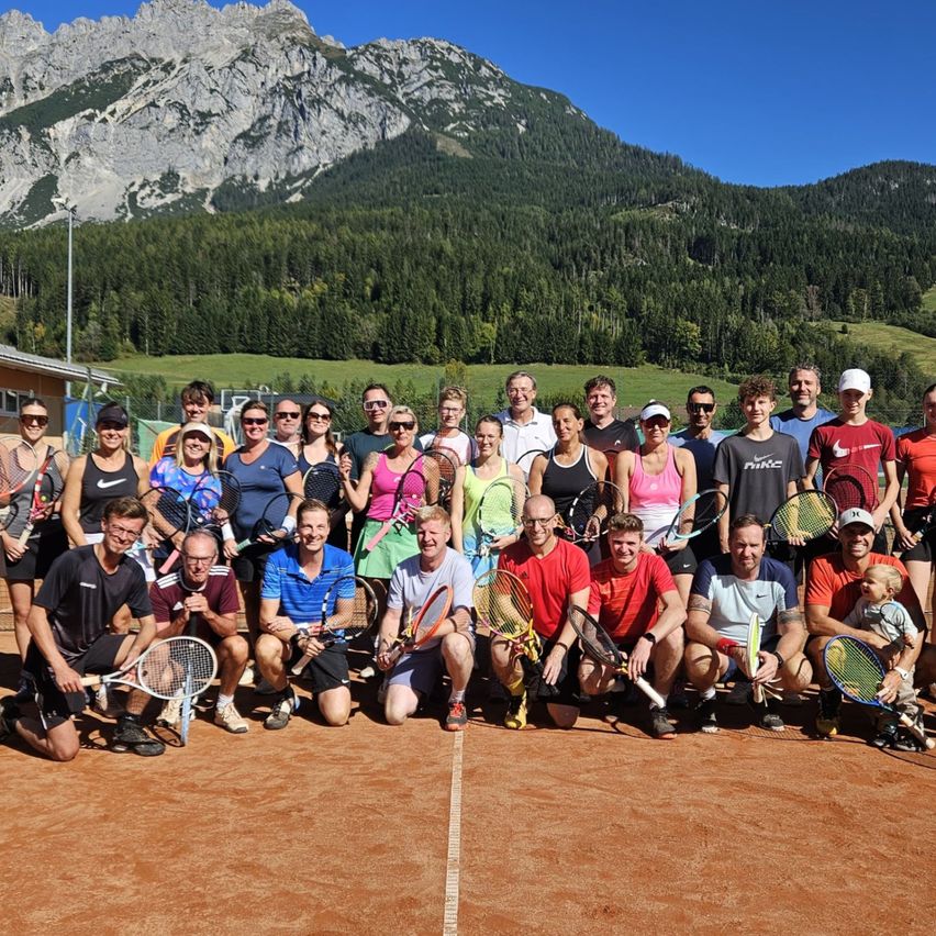 Eine Gruppe von Tennisspielern posiert für ein Foto auf einem Tennisplatz mit Bergen im Hintergrund.