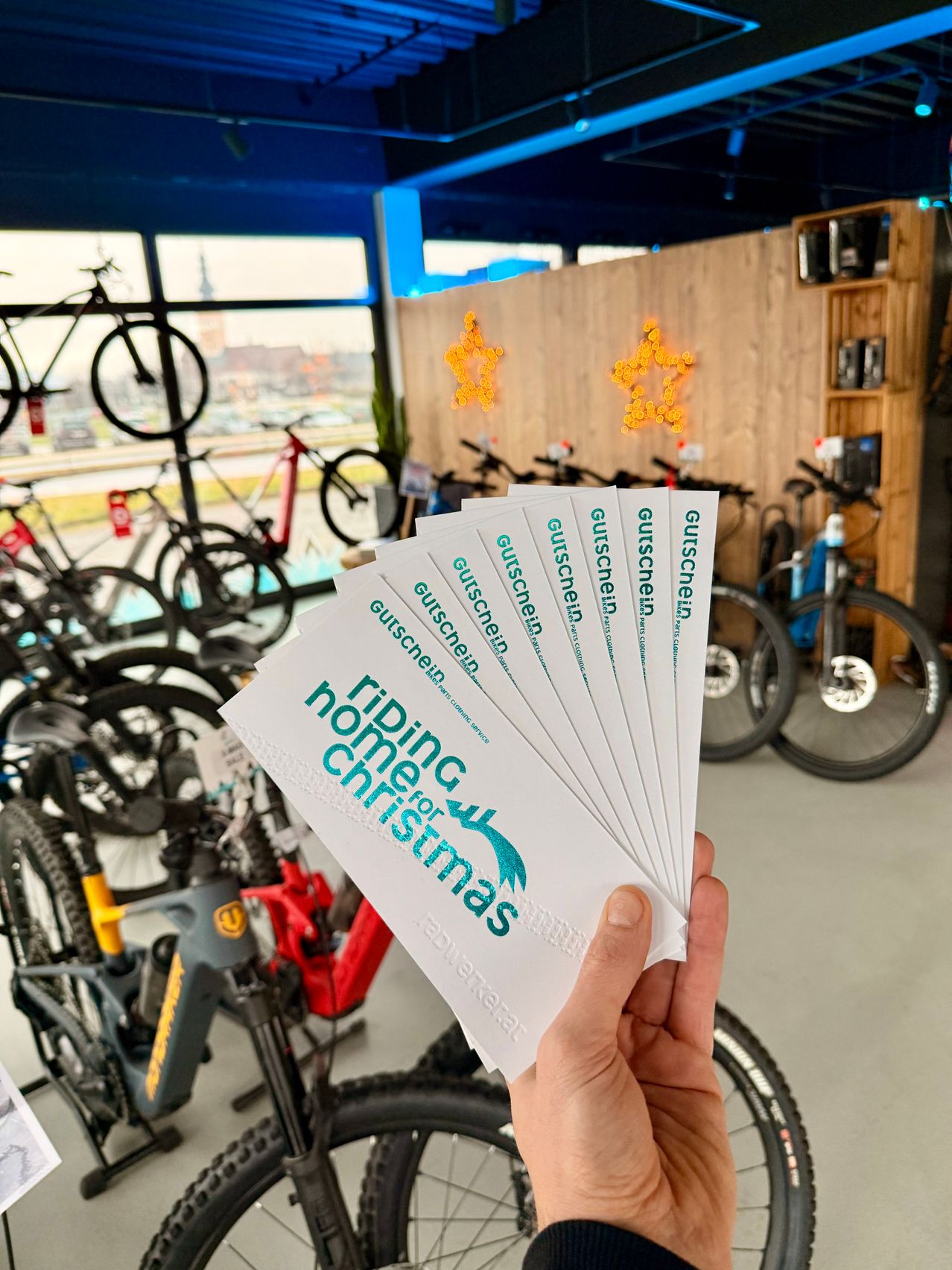 Eine Hand hält mehrere Geschenkgutscheine für ein Fahrradgeschäft, mit vielen Fahrrädern im Hintergrund.