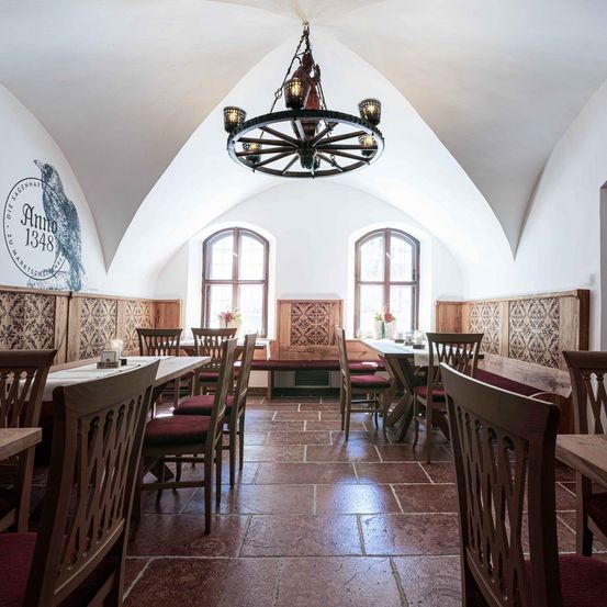 Ein Innenbereich zum Essen mit einer Kronleuchter, Holzstühlen und Tischen. Es gibt gewölbte Decken, gewölbte Fenster und eine Wand mit einer Eule und einem Datum.