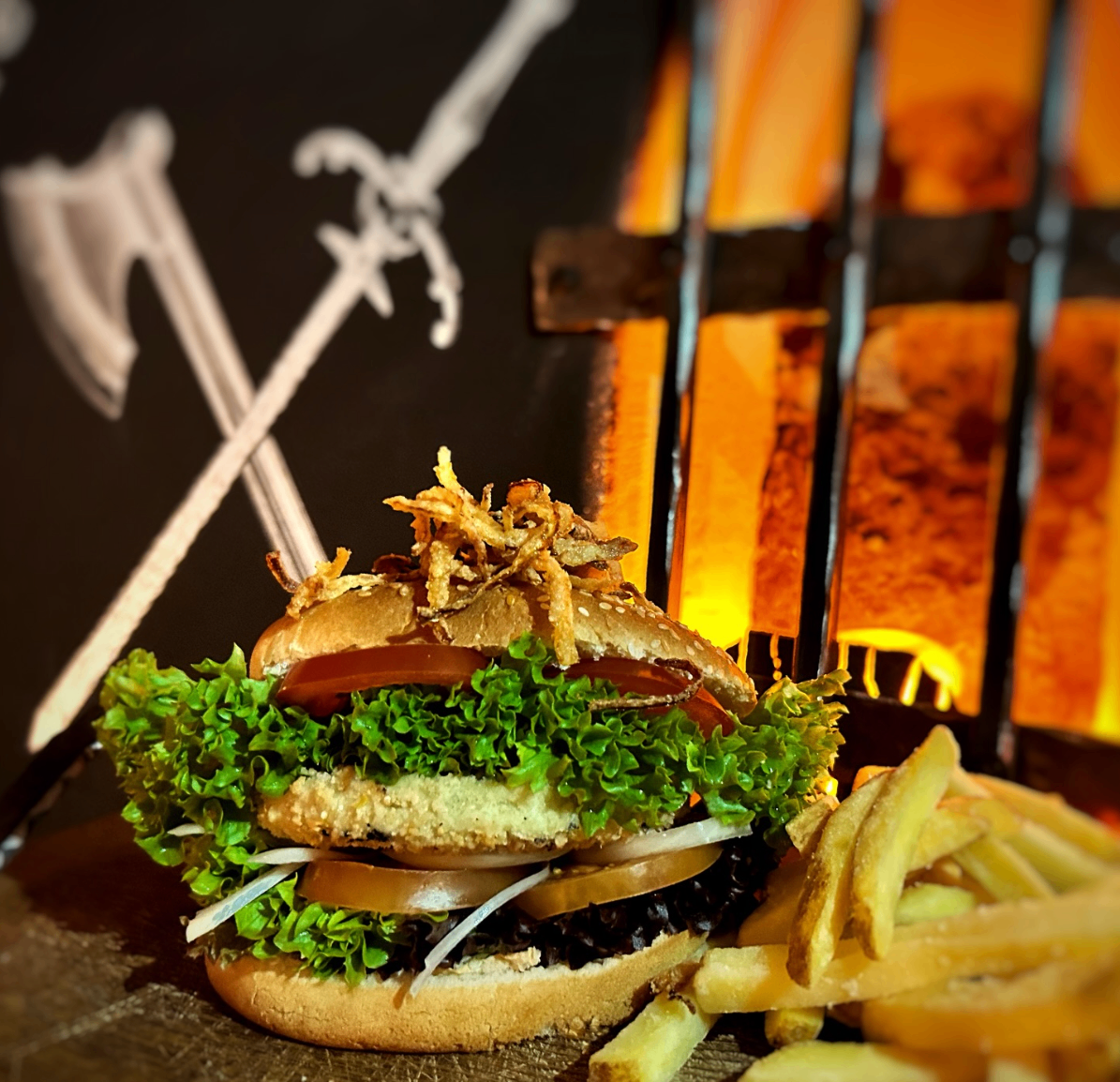 Ein Burger mit Salat, Tomate, Zwiebel und knusprigen Zwiebeln, serviert mit Pommes vor einem feurigen Hintergrund mit Schwertern.