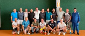 Eine Gruppe von Tennisspielern posiert für ein Foto in einer Sporteinrichtung, alle in Sportbekleidung und mit Tennisschlägern, vor einer grünen Wand.