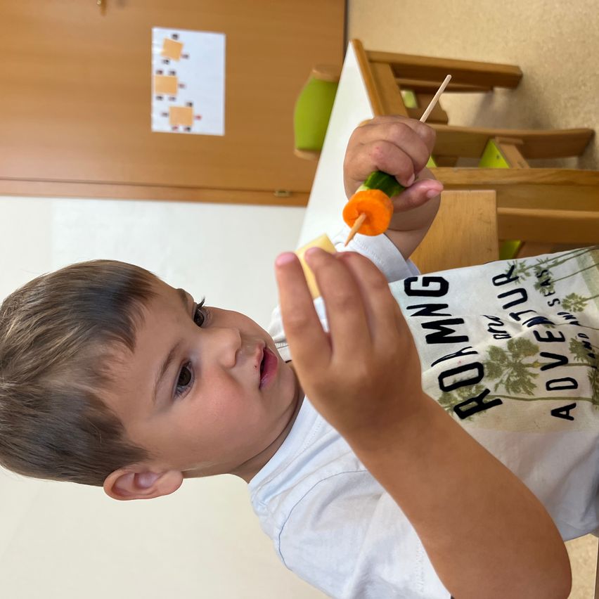 Ein junger Junge in einem weißen T-Shirt macht einen Gemüsespieß mit Karotte und Gurke.