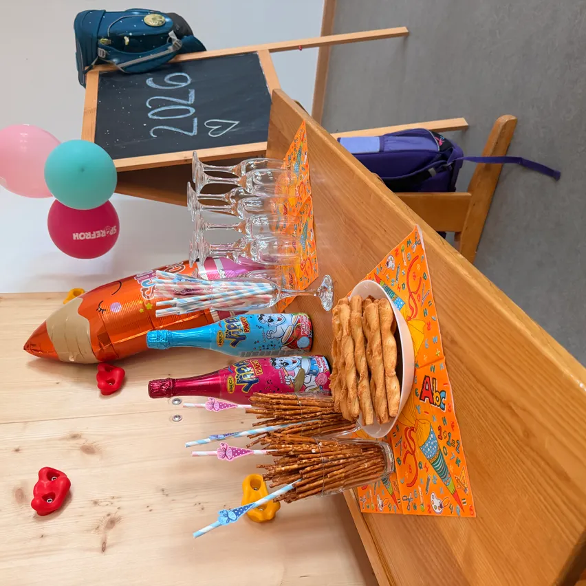 Ein Holztisch zeigt eine Geburtstagsdekoration mit Luftballons, einer Tafel mit dem Jahr 2020, einer Schüssel mit Brezeln und verschiedenen Flaschen.