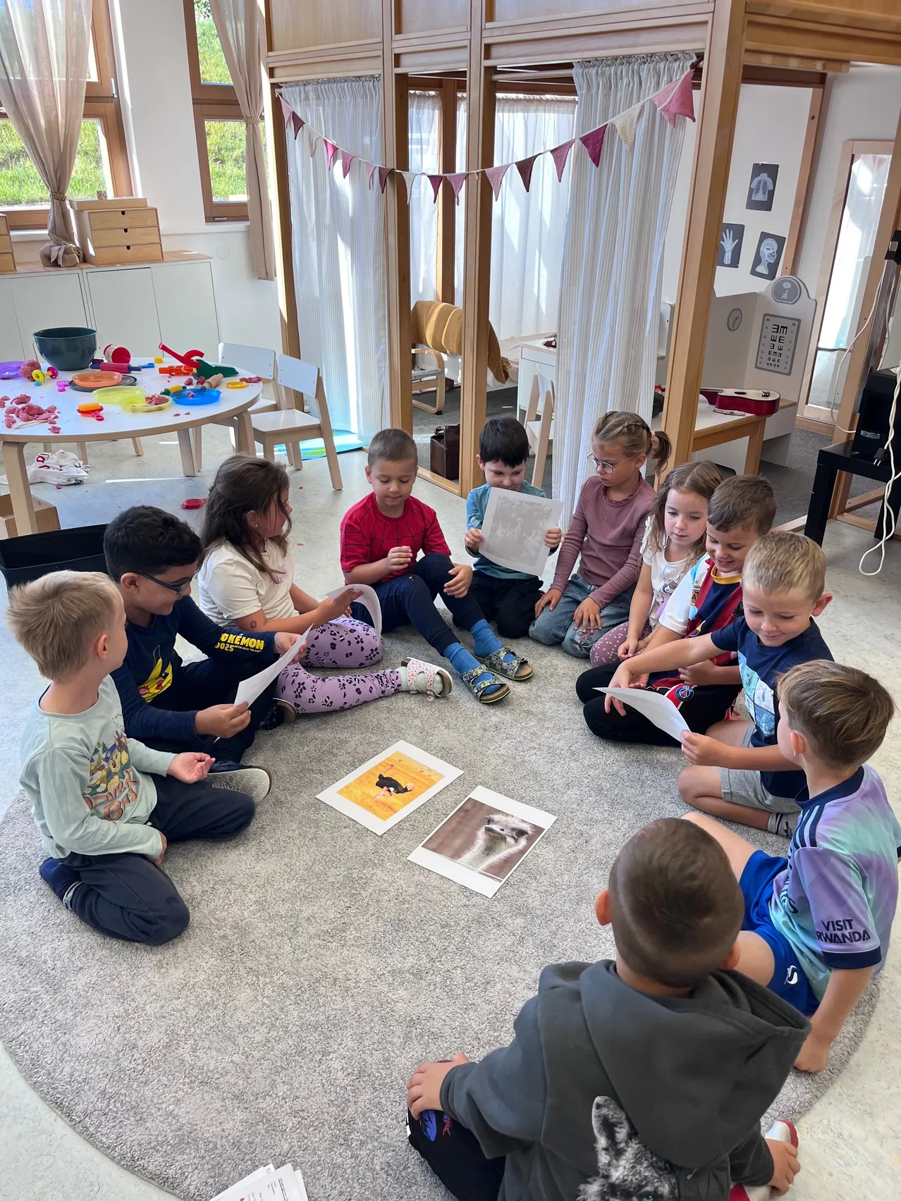 Eine Gruppe von Kindern sitzt im Kreis auf dem Boden und liest Papiere und schaut sich Bilder an.