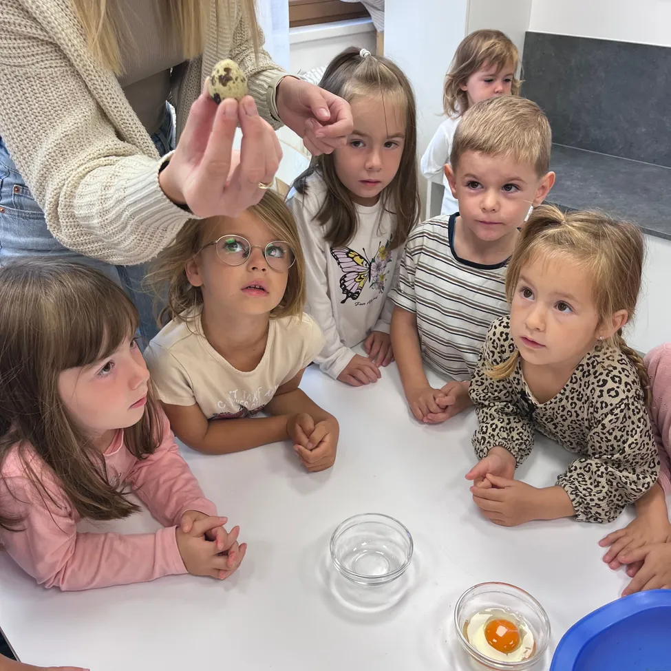 Eine Frau zeigt einem kleinen Ei einer Gruppe von Kindern, die um einen Tisch sitzen.