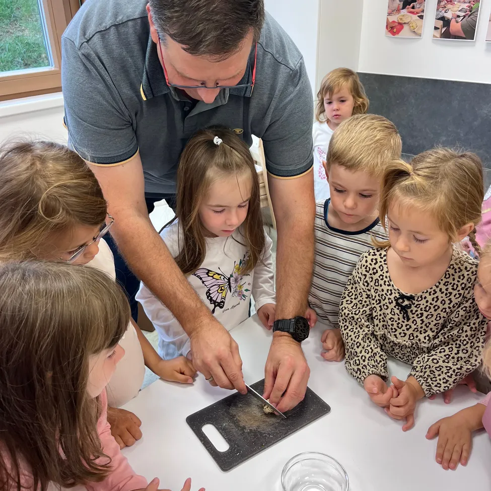 Ein Mann unterrichtet eine Gruppe junger Kinder, wie man ein Ei mit einem Messer auf einem Schneidebrett schneidet.