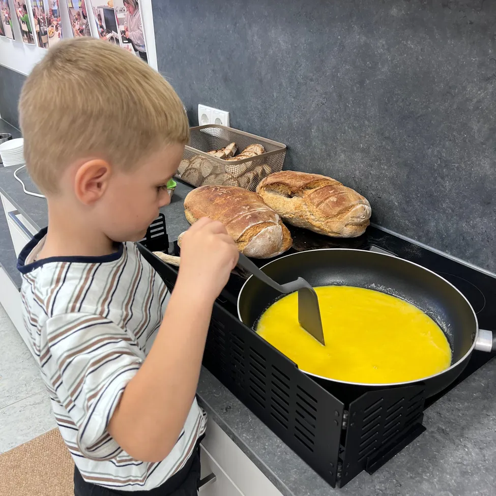 Ein junger Junge kocht in der Küche. Er hält eine Pfannenwender und ist dabei, das gelbe Essen in der Pfanne zu wenden.