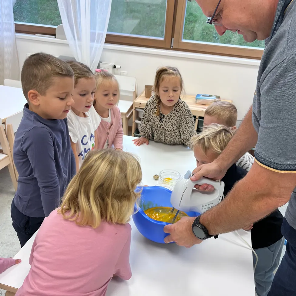 Ein Mann hilft Kindern, Zutaten in einer Schüssel mit einem Handmixer in einem Klassenzimmer zu mischen.