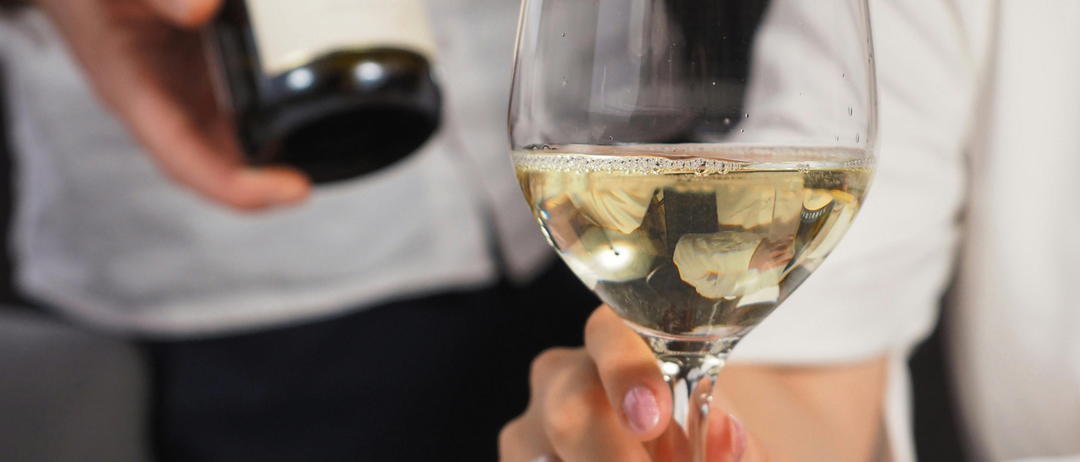 Eine Person hält eine Weinflasche in der linken Hand und ein Glas Weißwein in der rechten Hand. Die Weinflasche hat das Wort Serbien auf ihrem Etikett.