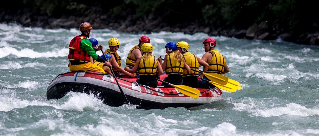 Eine Gruppe von Menschen treibt auf einem Fluss, trägt Helme und Schwimmwesten und paddelt durch das Wasser.