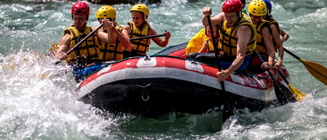 Eine Gruppe von Menschen treibt auf einem Fluss. Sie tragen alle gelbe Helme und Sicherheitswesten. Einige von ihnen halten Paddel.