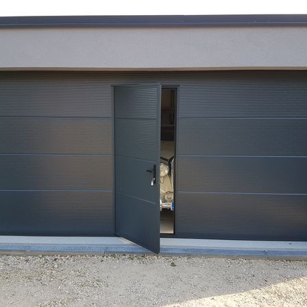 Ein offenes Garagentor zeigt einen Oldtimer im Inneren. Die Garage besteht aus geriffelten Paneelen und hat ein modernes Design.