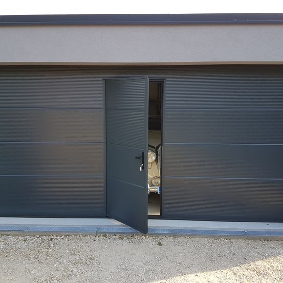 Ein offenes Garagentor zeigt einen Oldtimer im Inneren. Die Garage besteht aus geriffelten Paneelen und hat ein modernes Design.