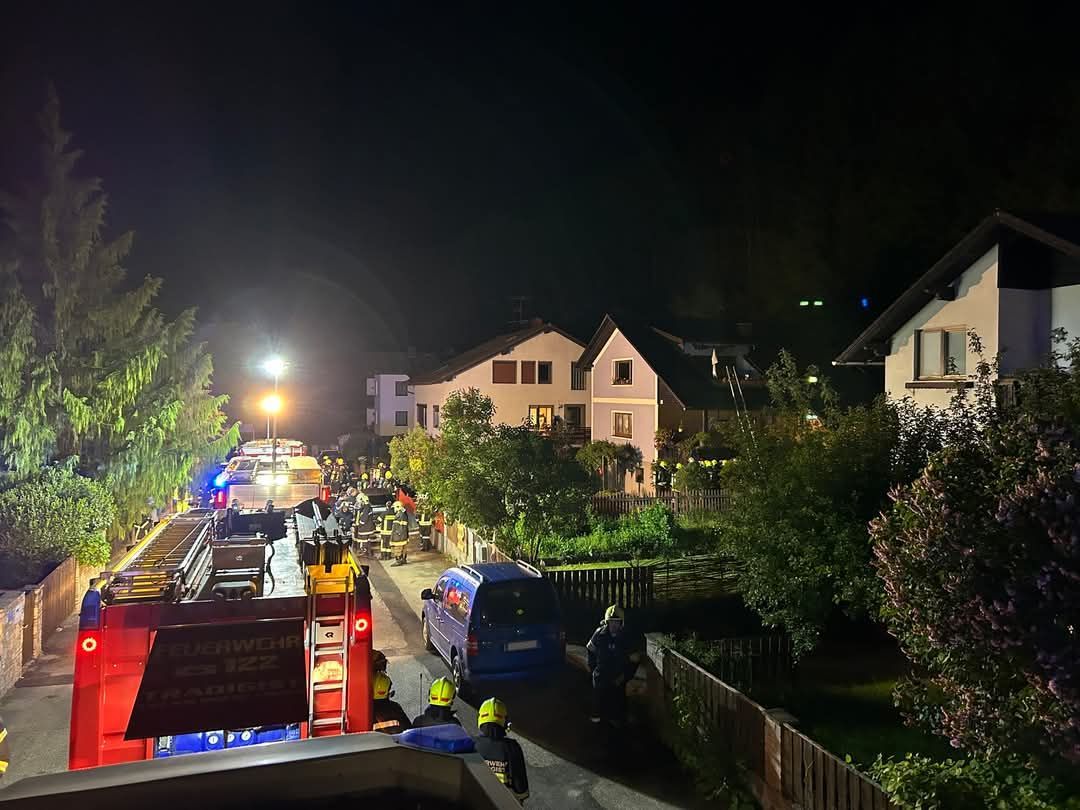 Ein Feuerwehrwagen und mehrere Feuerwehrleute sind nachts auf der Straße vor einem Haus geparkt.