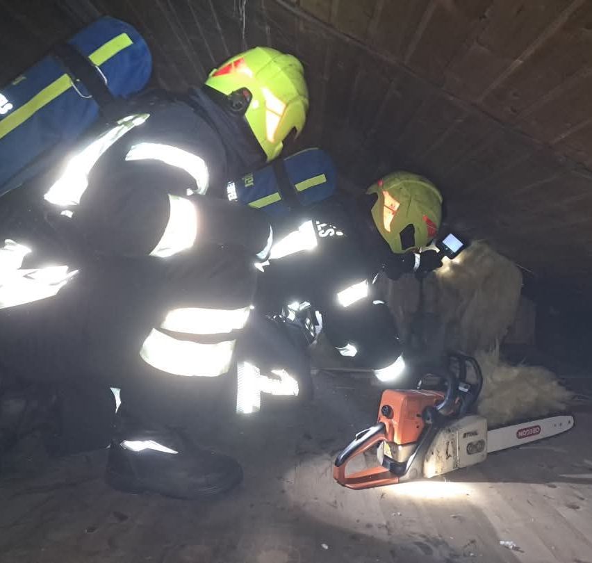 Zwei Feuerwehrleute in voller Ausrüstung arbeiten an einer Rettung in einem beengten Raum und sägen mit einer Kettensäge durch Trümmer.