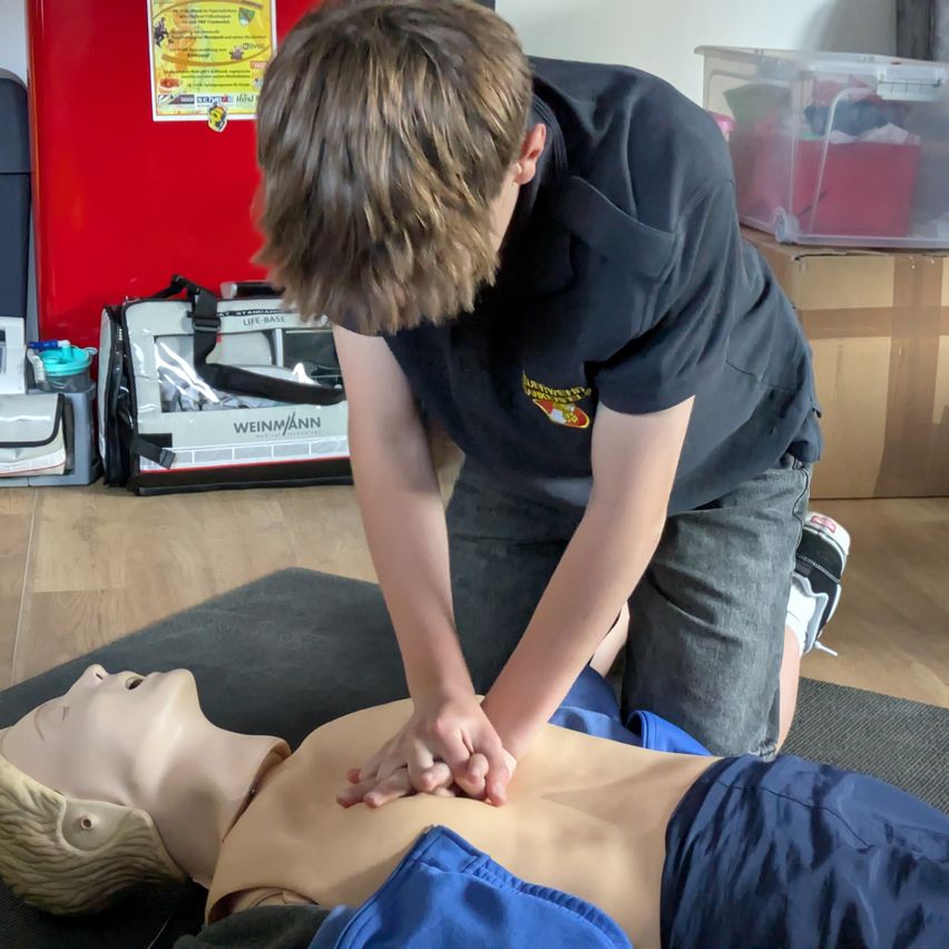Ein junger Junge übt CPR auf einem Dummies in einem Raum mit Holzböden.
