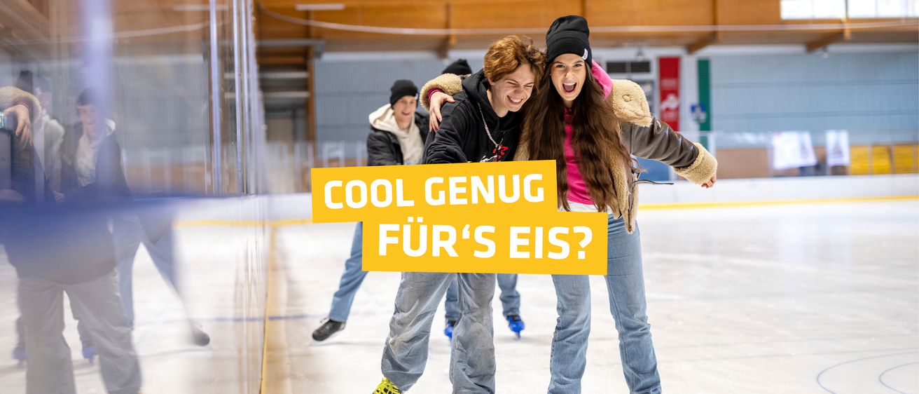 Drei junge Leute skaten auf einer überdachten Eisbahn, zwei Mädchen und ein Junge. Ein Mädchen hält ein Schild mit der Aufschrift 'Cool genug für's Eis?'.