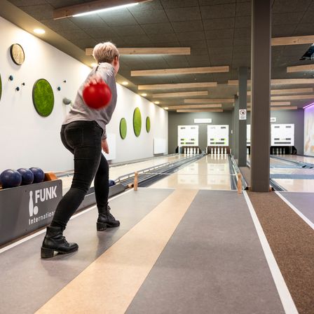 Eine Frau bereitet sich darauf vor, in einer Bowlingbahn mit modernem Design zu werfen, die mit Holzbalken und dekorativen Wandelementen ausgestattet ist.