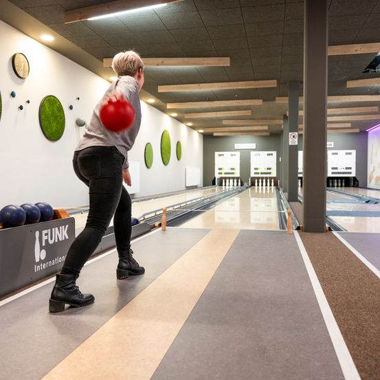 Eine Frau bereitet sich darauf vor, in einer Bowlingbahn mit modernem Design zu werfen, die mit Holzbalken und dekorativen Wandelementen ausgestattet ist.