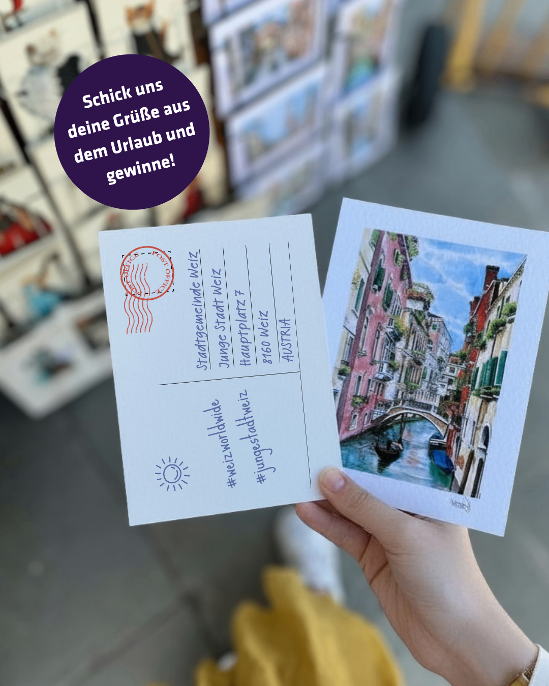 Eine Person hält zwei Postkarten, eine mit einer handgezeichneten Kanalszene und die andere mit einem Stempel und Text. Der Hintergrund zeigt einen Laden mit verschiedenen Artikeln.
