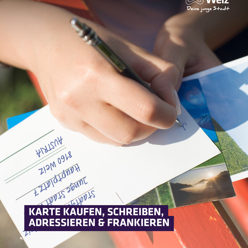 Eine Hand schreibt mit einem Stift auf ein Blatt Papier. Das Papier hat ein Postkartenbild im Hintergrund mit dem Text 'Karte kaufen, schreiben, adressen & frankieren'.