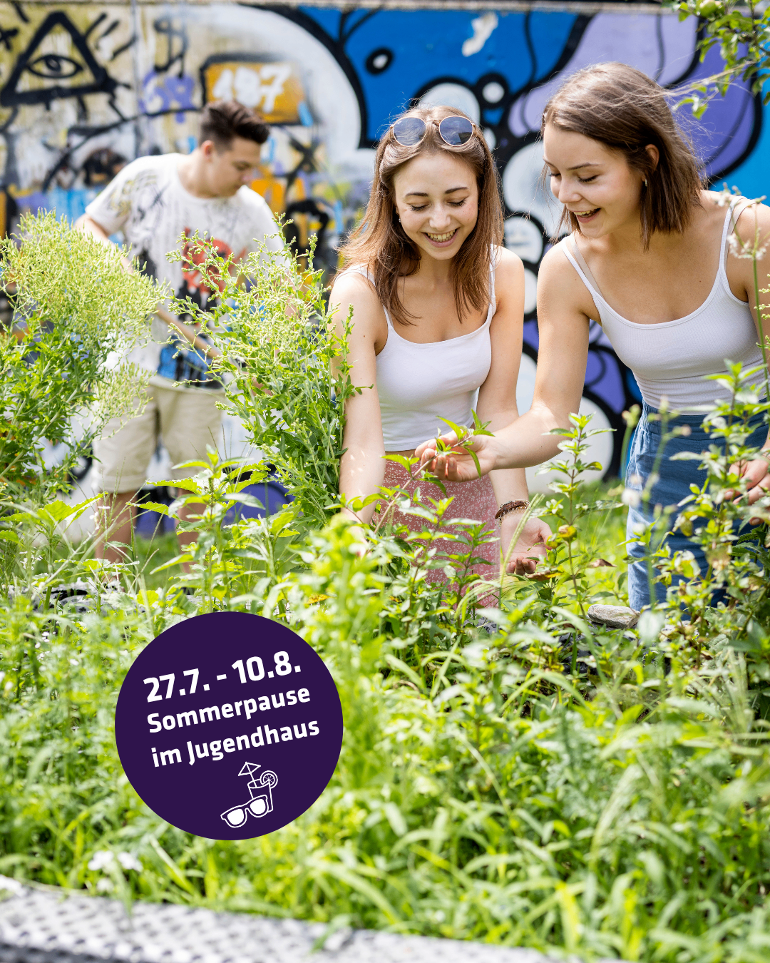 Drei junge Menschen sind im Garten. Zwei Frauen lächeln und betrachten Pflanzen, während ein Mann hinter ihnen steht. Der Garten ist von einer bunten Graffiti-Wand umgeben. Das Bild hat einen Wasserzeichen mit dem Text '27.7.-10.8. Sommerpause im Jugendhaus'.