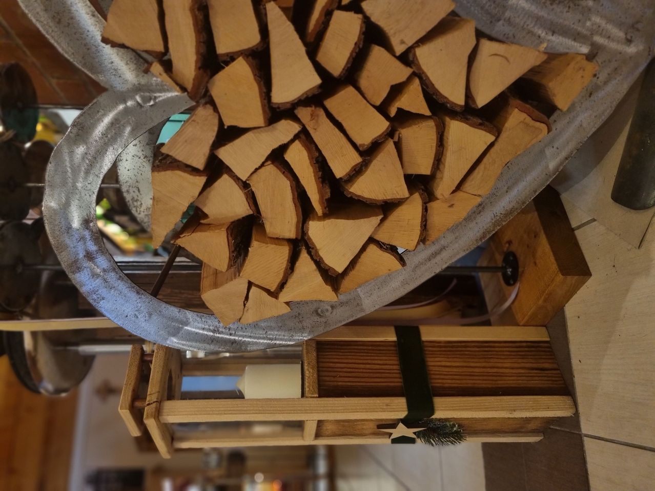 Ein großer Haufen gehackter Holzscheite in einem Metallbehälter mit einem dekorativen Holzkasten darunter.
