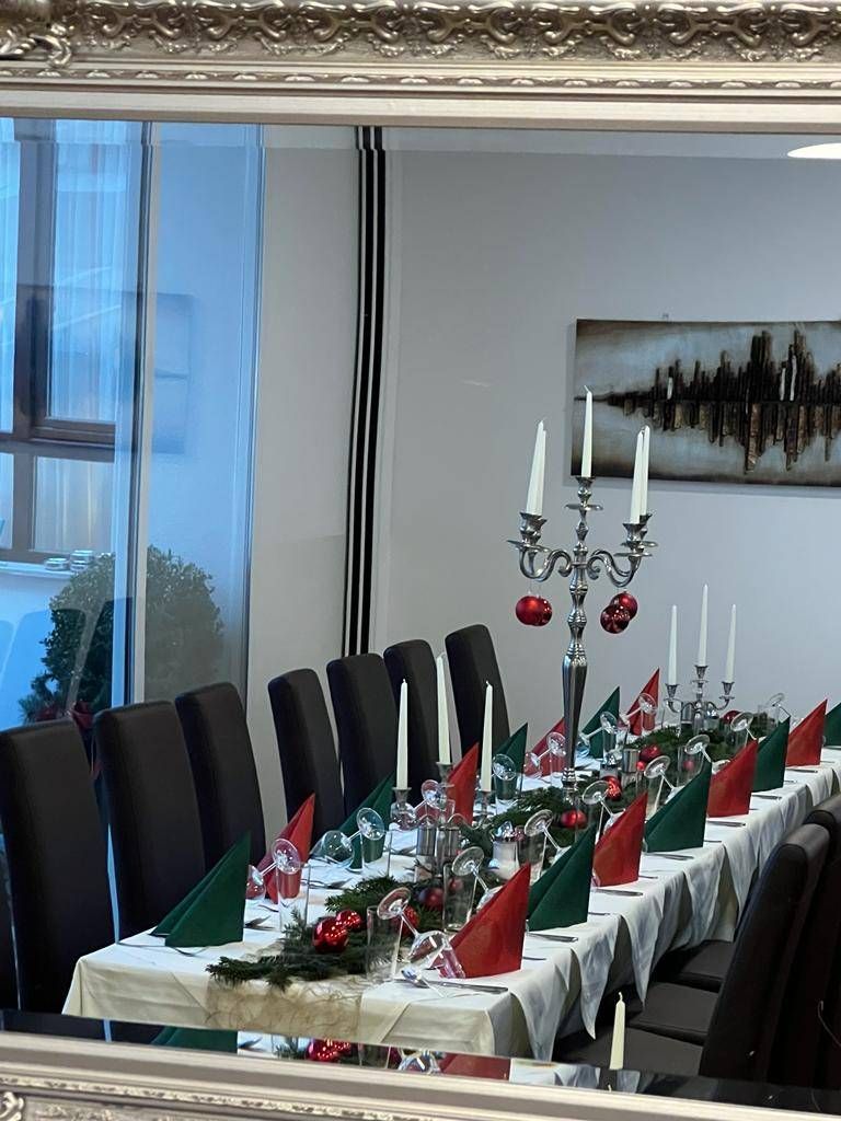 Ein langer Esstisch, geschmückt für eine Weihnachtsfeier, mit roten und grünen Servietten, Weingläsern und einem Weihnachts-Zentrenstück mit Kerzen und Ornamenten.