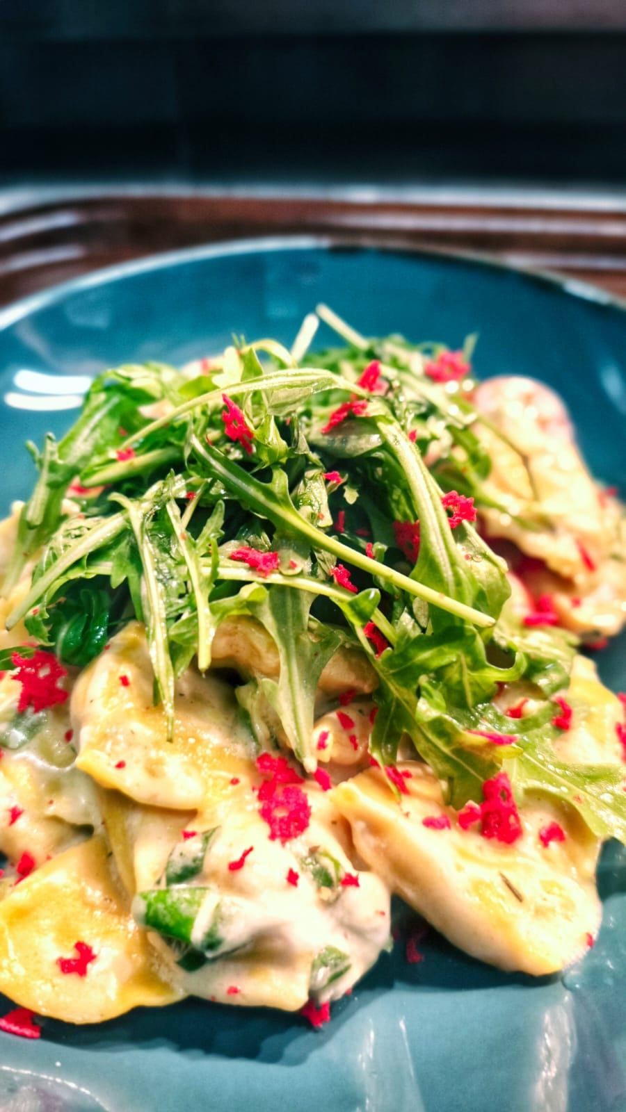 Ein Teller mit cremiger Pasta, über die Rucolablätter und rote Chiliflocken gestreut sind. Das Gericht wird auf einem blauen Teller serviert.
