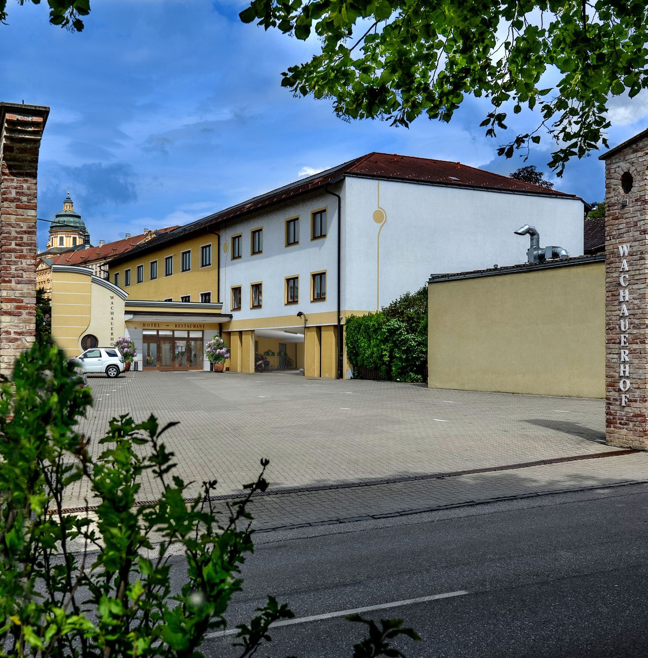 A white and yellow building with a brown roof stands in front of a parking lot, with a white car parked in front.