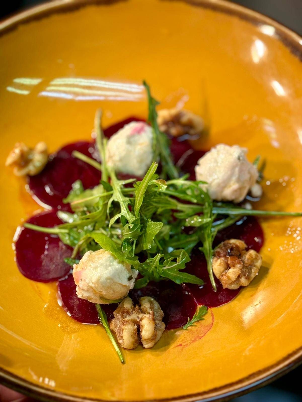 A vibrant yellow plate with a salad of sliced beets, arugula, and crumbled cheese, garnished with toasted walnuts.