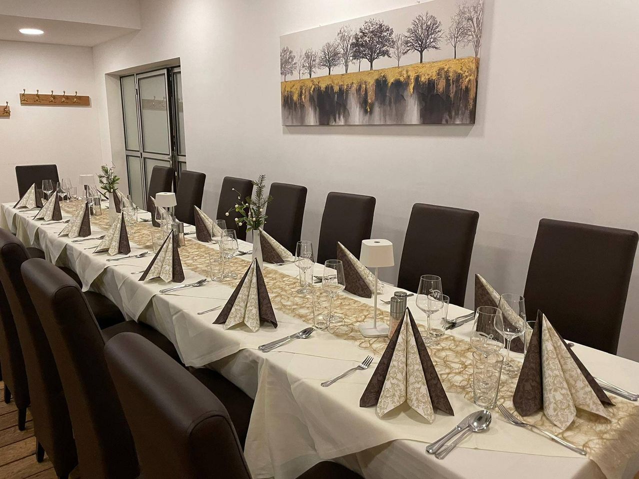 Ein langer Esstisch, der für eine Mahlzeit mit dekorativen Servietten und Besteck vorbereitet ist, mit einem Landschaftsgemälde an der Wand.