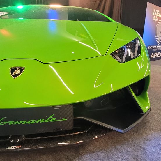 Ein lindgrüner Lamborghini Huracán wird mit einem grünen Lamborghini-Logo auf dem vorderen Stoßfänger ausgestellt. Die Scheinwerfer sind eingeschaltet und das Auto befindet sich in einem exklusiven Autoshow-Bereich.