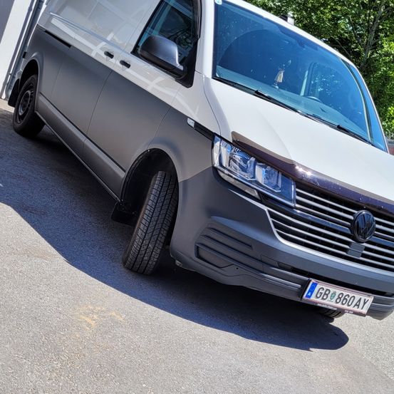 Ein grauer Volkswagen-Transporter ist am Straßenrand geparkt. Der Transporter hat ein Nummernschild GB860AY und ein Volkswagen-Logo auf der vorderen Stoßstange.