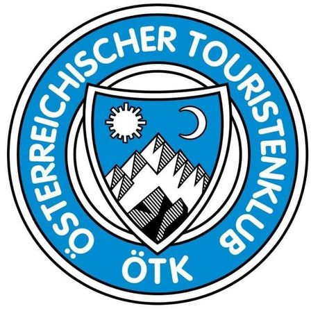 Das Logo des Österreichischen Touristenklubs ist kreisförmig mit blauen und weißen Farben. Es zeigt einen Schild mit einer Bergkette und einer Sonne und einem Mond in der Mitte. Der Text lautet 'Osterreichischer Touristenklub'.