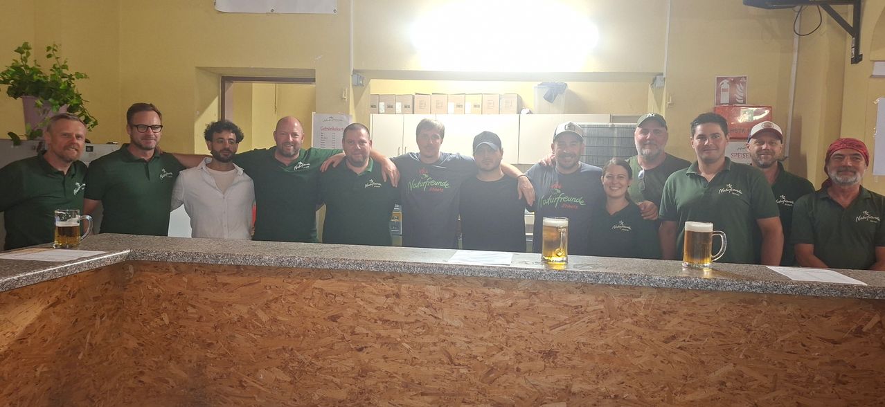 Eine Gruppe von Menschen in grünen Shirts lächelt und posiert für ein Foto in einer Bar mit einem Glas Bier.