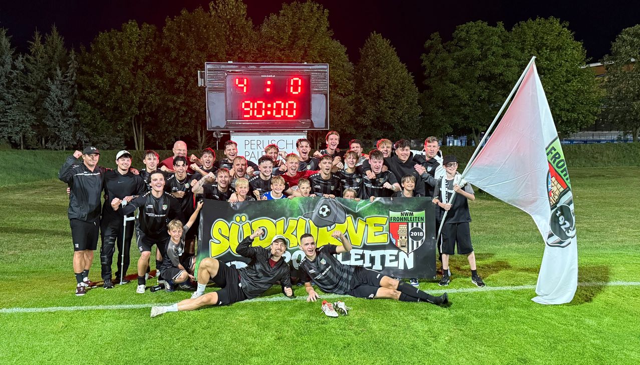 Eine Fußballmannschaft feiert mit einem großen Banner auf einem Feld, mit einem Spielstand von 4:0 im Hintergrund.