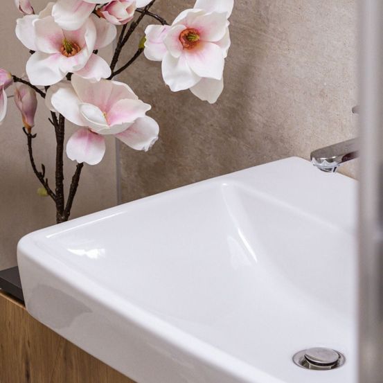 Ein weißes Waschbecken im Badezimmer mit silbernem Wasserhahn und einem Strauß rosa und weißer Magnolienblüten.