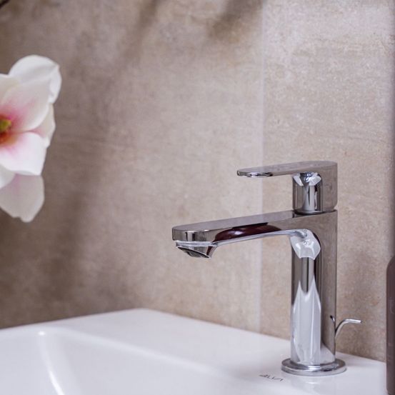 Ein weißes Badezimmerbecken mit einem modernen Chrom-Wasserhahn und einer dekorativen rosa Blume in der Nähe an der Wand.