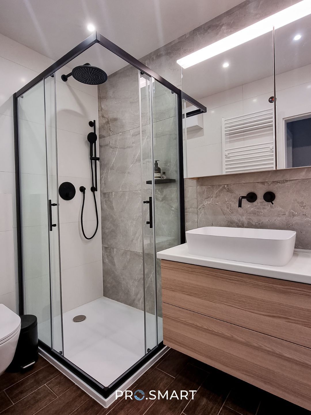 A modern bathroom with a glass shower stall, black fixtures, a white sink, and wooden cabinetry.