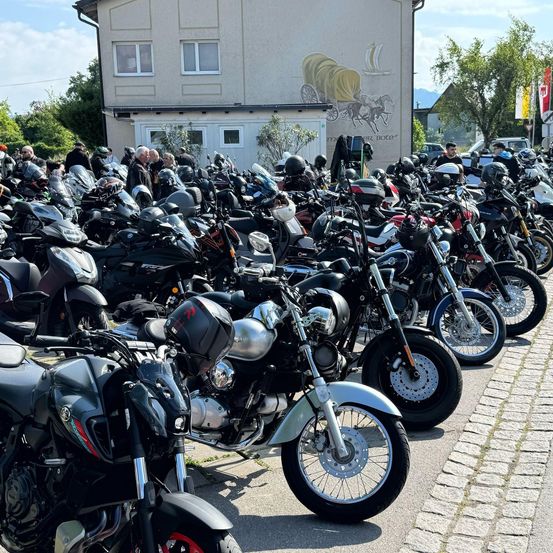 Eine große Gruppe von Motorrädern ist vor einem Gebäude mit einem Wandbild geparkt. Leute stehen herum, einige tragen Helme.