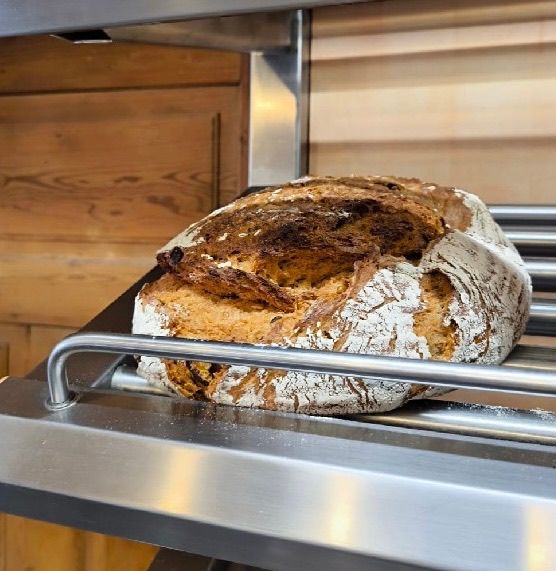 A loaf of bread is on a baking sheet in an oven. The oven has wooden cabinets and stainless steel handles.