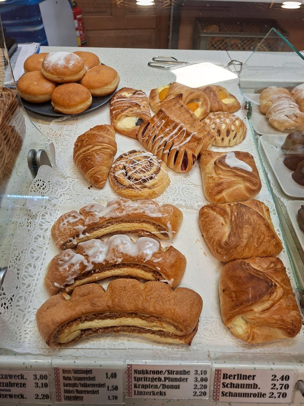 Eine Auswahl an Gebäck wie Croissants, dänisches Gebäck und Donuts, auf einem Tresen präsentiert mit verschiedenen Toppings und Glasuren.