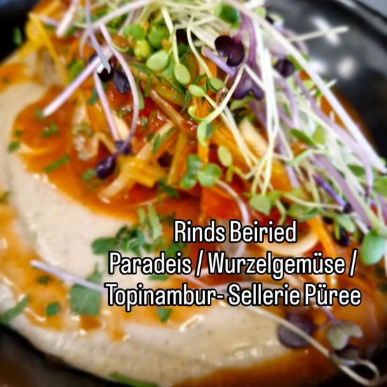 Ein Nahaufnahme eines Gerichts mit cremiger weißer Basis, überzogen mit bunten Gemüsen, Sprossen und einer roten Sauce. Das Gericht ist mit Mikrogrün und Kräutern garniert.