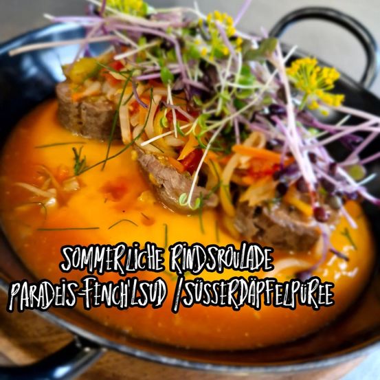 Eine Schüssel mit sommerlichem Fenchelsud mit Fleisch und garniert mit Microgreens und gelben Blumen, beschriftet 'Sommerliche Rindsroulade Paradis-Fenchelsud / Susserdappelpuree'.